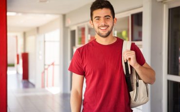Portrait of a Hispanic college student carrying a backpack and standing in a school hallway